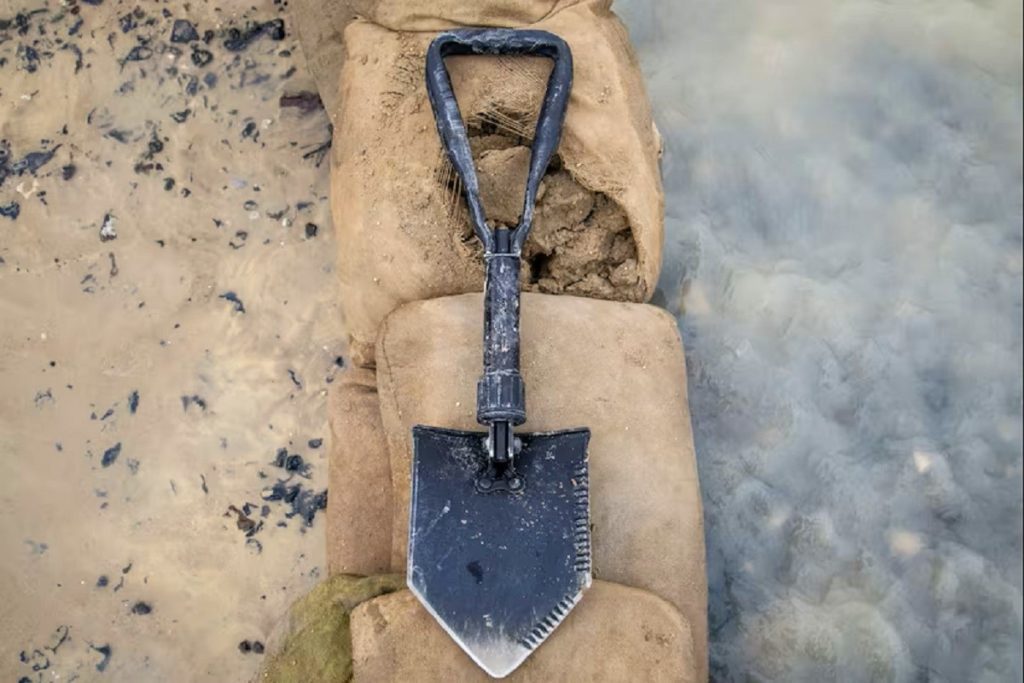 An e-tool sits atop sandbags with one side flooded, and the other side dry