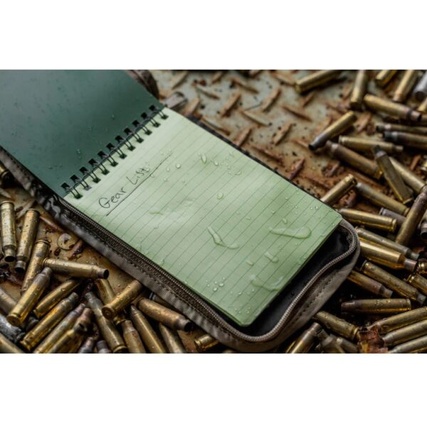 a green and yellow waterproof notebook resting on top of bullet casings