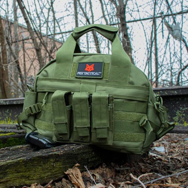 an olive drab (green) gun, ammo, and accessory shooting range bag resting on old railroad tracks